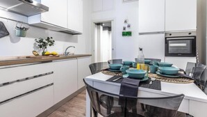 A modern kitchen with white cabinets, a stainless steel range hood, and a dining area with a glass table and blue bowls. - Elegant & Spacious 3-Bedroom Apartment in Milan’s Historic Center (Milano)