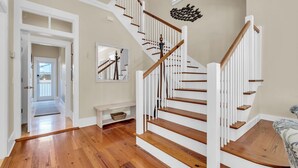 Un interior espacioso con una escalera de madera, un banco y vistas a un pasillo.