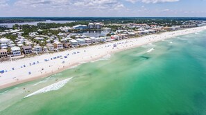 An aerial view of a beach with a row of beachfront hotels, clear turquoise waters, and a sandy shore. - Calliope: Across from Carillon Beach Walkover #1 w/ Huge Outdoor Balcony (Panama City Beach)