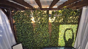 A cozy outdoor seating area with a cushioned bench and a chair, surrounded by a lush green hedge. - Cosy 1BR Hideaway - Hot Tub, Wifi & Private Pond (Newark)