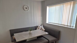 A modern living room with a grey sofa, a wooden dining table, and a potted plant. - Cosy 1BR Hideaway - Hot Tub, Wifi & Private Pond (Newark)