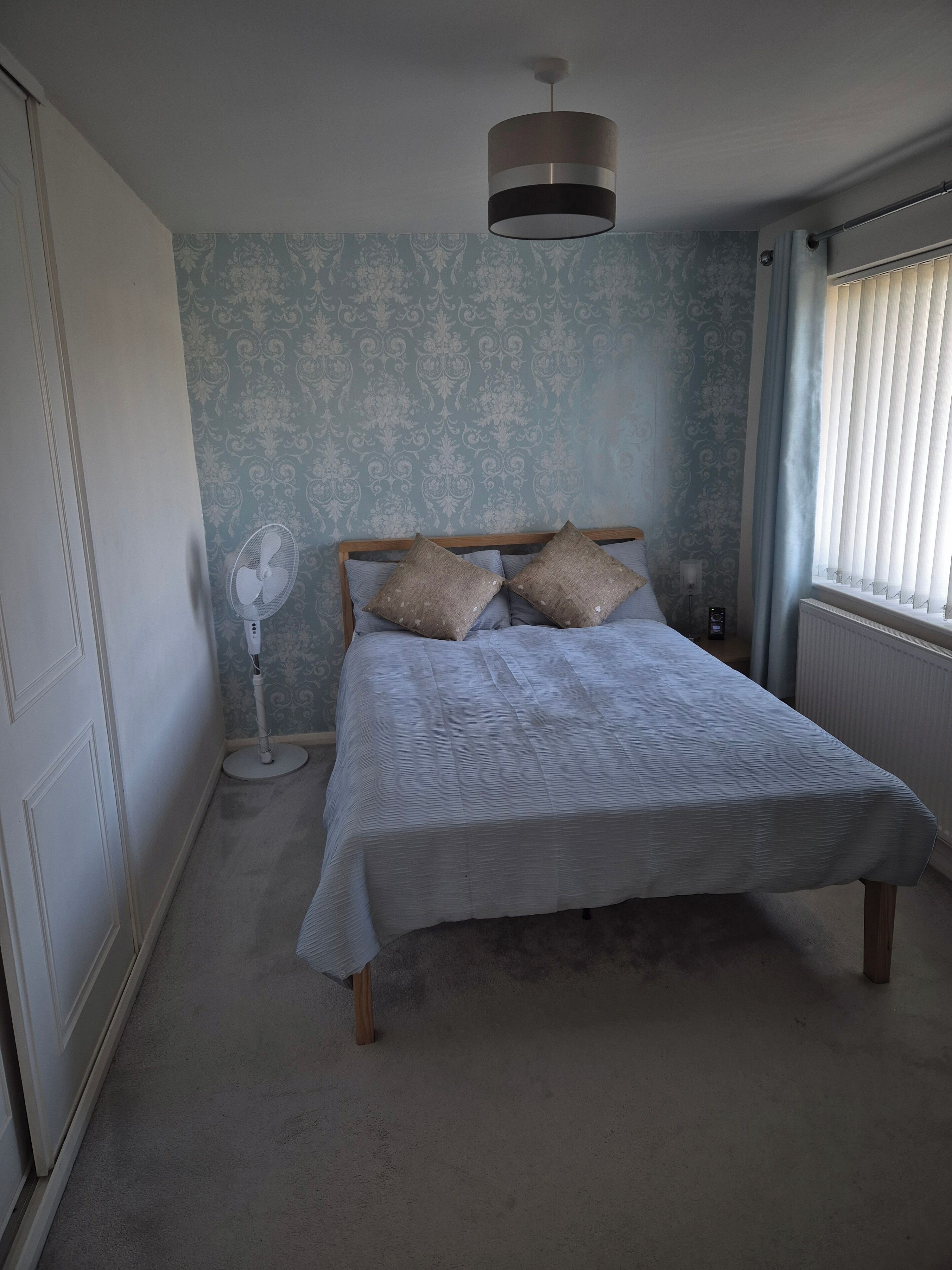 A bedroom with a bed, a standing fan, and a ceiling light.
