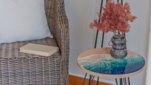 Un canapé en osier agrémenté d’un coussin blanc et une petite table en bois sur laquelle sont posés un vase en verre et une assiette décorative.