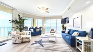Ein großzügiges Wohnzimmer mit einem großen Fenster, einem Deckenventilator und einem blauen Sofa.