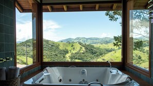 A bathroom with a large bathtub, a window with a view of green hills, and a wooden ceiling. - Lavandas de Cunha Pousada Boutique (Cunha)