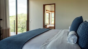 A bedroom with a large bed, a view of the outdoors through a sliding door, and a bathroom visible through an open door. - Lavandas de Cunha Pousada Boutique (Cunha)