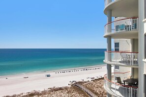 Ein Strandhotel mit Balkon und Meerblick, ein Sandstrand und ein klarer Himmel.