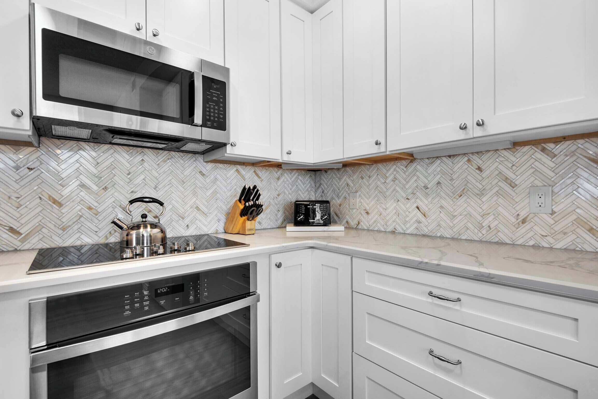 Uma cozinha moderna com armários brancos, micro-ondas, forno e chaleira na bancada.