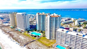 A high-rise hotel with multiple balconies, a central courtyard with a pool, and a view of the sea. - 🏝️Huge Balcony w/Gulf Views ☀️ Beach Colony Resort East 11A (Navarre Beach)