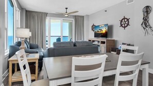 A modern living room with a dining area, large windows, and a view of the sea. - 🏝️Huge Balcony w/Gulf Views ☀️ Beach Colony Resort East 11A (Navarre Beach)
