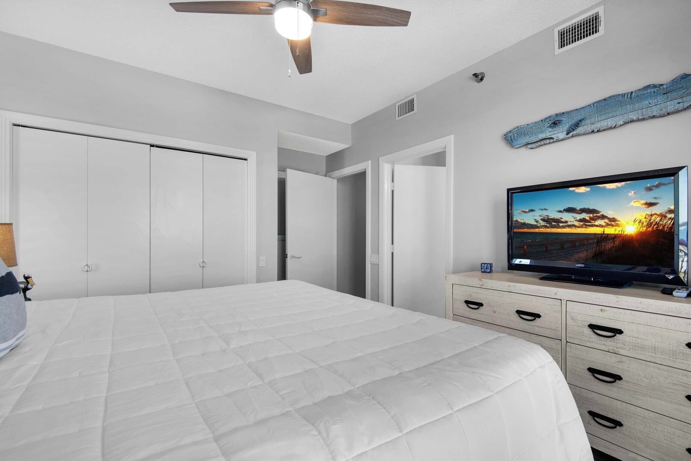 Ein Schlafzimmer mit Bett, Deckenventilator, Fernseher und einem hölzernen Schminktisch.