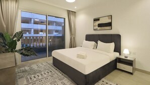 A hotel room with a bed, a nightstand, a lamp, a large window with curtains, and a potted plant.