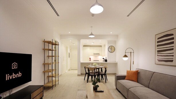 A modern living room with a flat-screen TV, a sofa, a coffee table, and a dining area with chairs and a table.