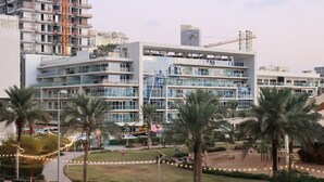 Um hotel moderno com vários andares, janelas amplas e um pátio central com palmeiras.