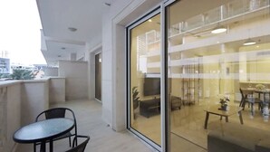 A balcony with a table and chairs, a sliding glass door leading to an interior space with a dining area and a sofa.
