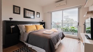 Un dormitorio moderno con una cama grande, una mesita de noche, un escritorio y una ventana con vistas a la ciudad.