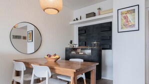Un comedor con mesa de madera, sillas blancas, un espejo y una pared de acento negra.