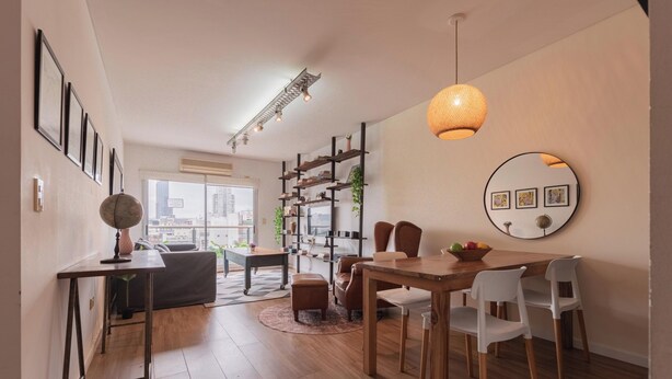 Una sala de estar moderna con zona de comedor, que presenta piso de madera, un espejo redondo y una estantería.