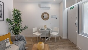 A modern hotel room with a dining area, a large mirror, an air conditioning unit, and a door with a 'SALIDA' sign. - Waou Coosy Retiro (Madrid)