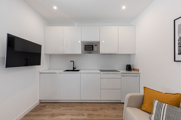 A compact kitchen with white cabinets, a microwave, a sink, and a dishwasher. - Waou Coosy Retiro (Madrid)