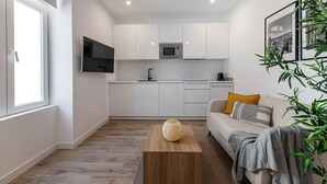 A modern kitchen with white cabinets, a microwave, and a sink. There's a wooden coffee table with a vase, a sofa with cushions, and a potted plant. - Waou Coosy Retiro (Madrid)