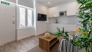 A modern kitchen with white cabinets, a microwave, and a TV. There's a wooden coffee table with a decorative vase. - Waou Coosy Retiro (Madrid)