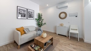 A modern living room with a sofa, a coffee table with books, a potted plant, and a small white table with a decorative item. - Waou Coosy Retiro (Madrid)