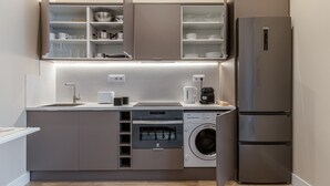 A compact kitchen with a built-in washing machine, a coffee maker, and a stainless steel refrigerator.