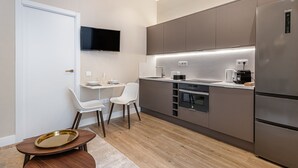 A modern kitchen with a flat-screen TV, stainless steel appliances, and a dining area with a small table and chairs.