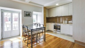 Una cocina moderna con armarios blancos, un horno de acero inoxidable y una zona de comedor con mesa y sillas de vidrio.