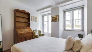Un dormitorio con una cama grande, cómoda de madera y dos ventanas.