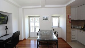 Un comedor con una mesa y sillas de vidrio, un televisor en la pared y una cocina con armarios y un fregadero.