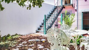 Un patio con pared blanca, una escalera y mobiliario exterior.
