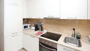 Una cocina compacta con armarios blancos, un microondas, un tostador, una tetera y un lavabo.