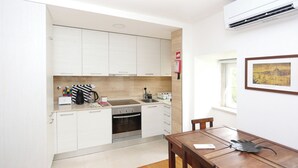 Cocina compacta con armarios blancos, horno integrado y comedor con mesa y sillas de madera.