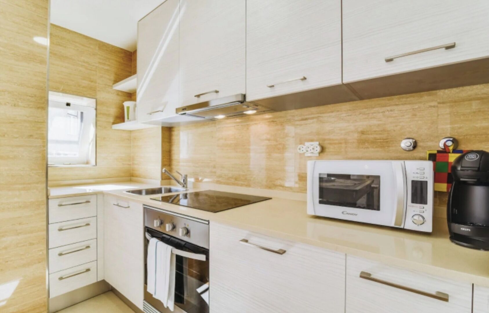 A compact kitchen with white cabinetry, a built-in oven, a microwave, and a coffee maker.