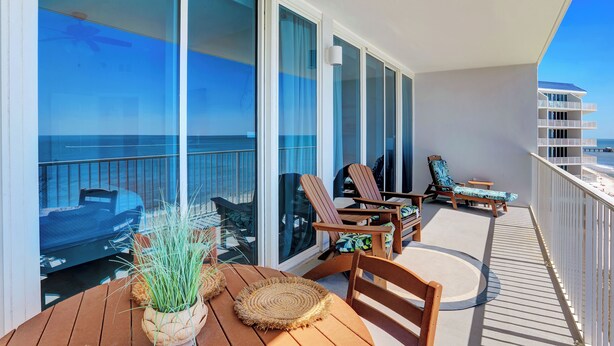 A balcony with a view of the ocean, wooden furniture, and a ceiling fan.