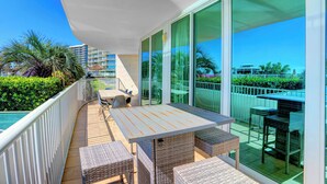 Un balcón con mesa y sillas, ventanas amplias y vistas del entorno.