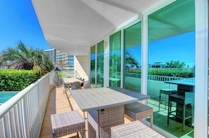 Un balcón con mesa y sillas, ventanas amplias y vistas del entorno.