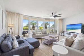 Ein modernes Wohnzimmer mit einem Ecksofa, einem Couchtisch und einem Fernseher, der einen Strandblick zeigt.