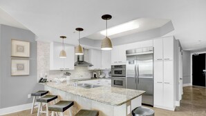 Una cocina moderna con armarios blancos, encimera de granito, electrodomésticos de acero inoxidable e iluminación colgante.