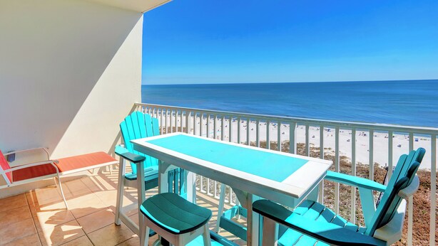 Ein Balkon mit Tisch und Stühlen, der auf einen Strand mit weißem Zaun und den Ozean blickt.