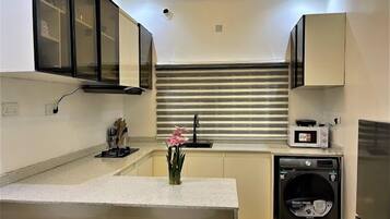 A compact kitchen with a built-in microwave, a coffee machine, and a washing machine.