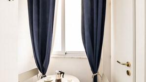Un baño con lavamanos blanco, cafetera y ventana con cortinas.
