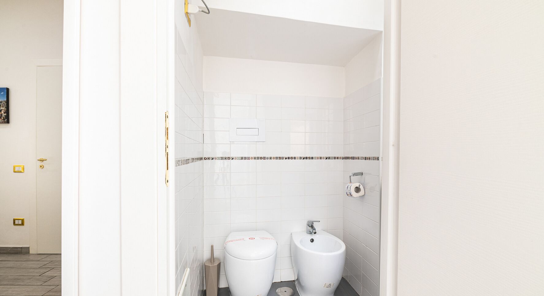 A bathroom with white tiled walls, a toilet, and a sink.