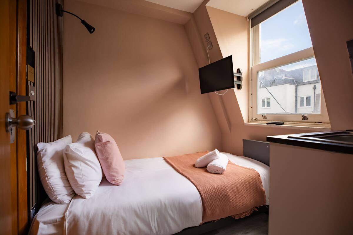 Un dormitorio con cama, almohadas, televisión y ventana.