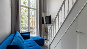 A modern living room with a blue sofa, a flat-screen TV mounted on the wall, and a staircase leading to another floor. - Britannia Hyde Park Hotel By PLI (London)