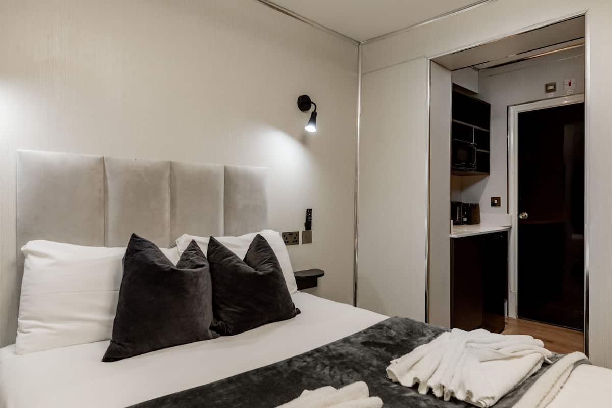 Una habitación de hotel con cama, almohadas, una mesita de noche y un armario.