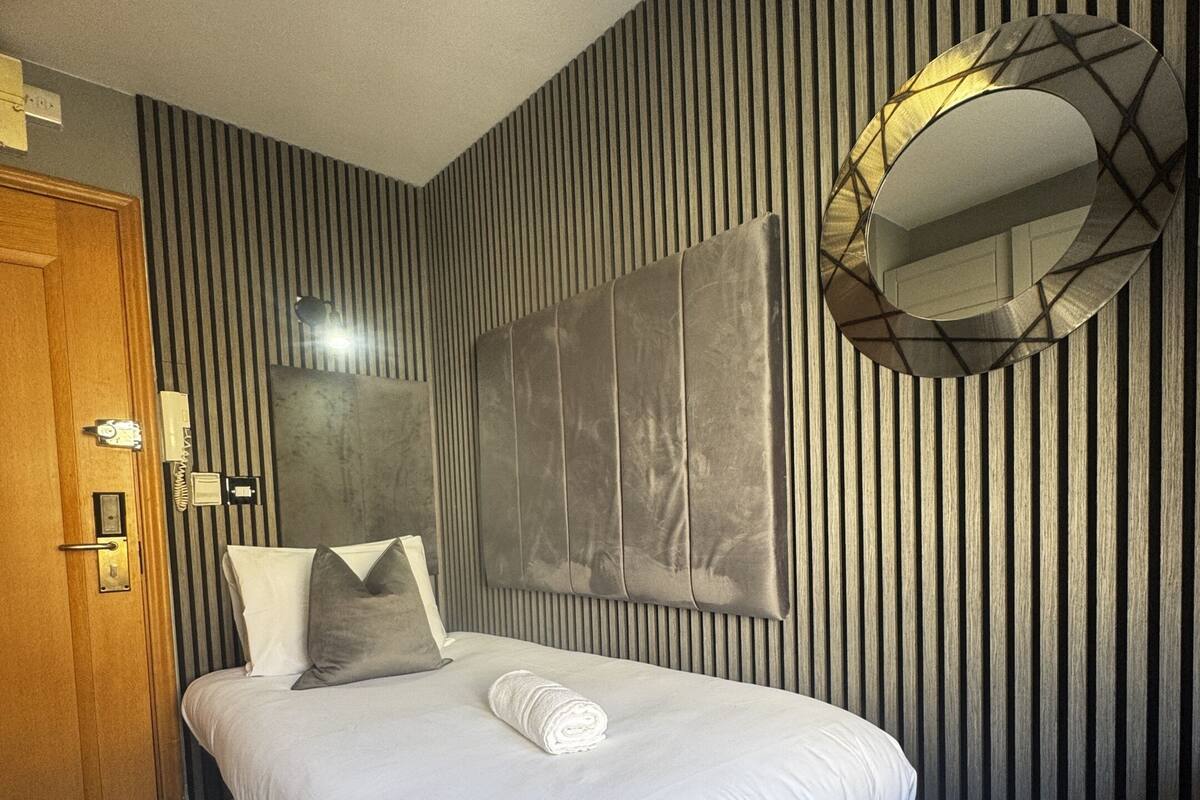 Un dormitorio moderno con una cama, un espejo redondo y una pared a rayas.