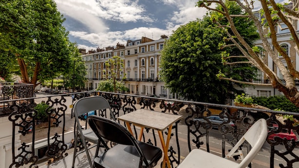 A balcony with two chairs and a table, overlooking a street with parked cars and buildings. - Britannia Hyde Park Hotel By PLI (London)